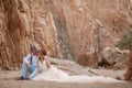 Bride and groom sit and smile in canyon on background of rocks. Royalty Free Stock Photo