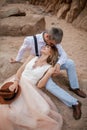 Bride and groom sit and smile on sand in canyon against background of rocks. Closeup. Royalty Free Stock Photo