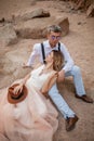 Bride and groom sit and smile on sand in canyon against background of rocks. Closeup.