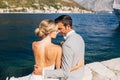 The bride and groom are sitting embracing on the pier in the Bay of Kotor, in front of them is the old town, close-up Royalty Free Stock Photo