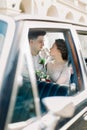 Bride with groom sitting in old black retro car. Newlyweds kissing and embracing while sitting inside old black retro car in old Royalty Free Stock Photo