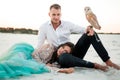 Bride and groom with small owl are sitting in desert on background of white sand. Closeup. Royalty Free Stock Photo