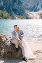 Bride and groom sit embracing against background of stones at the Lago di Braies in Italy. Destination wedding in Europe Royalty Free Stock Photo