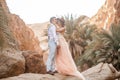Bride and groom stand and hug in canyon against background of rocks and palm trees.