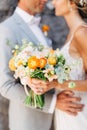 The bride and groom stand hugging at a brick wall in the old city and hold a wedding bouquet with orange flowers, close Royalty Free Stock Photo
