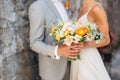 The bride and groom stand hugging at a brick wall in the old city and hold a wedding bouquet with orange flowers, close Royalty Free Stock Photo