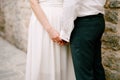 The bride and groom stand near a stone wall and touchingly hold each other& x27;s hands, close-up Royalty Free Stock Photo