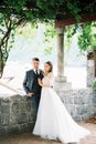 Bride and groom stand in a stone gazebo covered with ivy