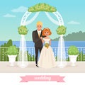 Bride and groom standing under floral arch. Wedding day. Couple in love. Woman in white dress, man in classic suit. Sea Royalty Free Stock Photo