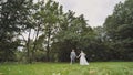 The bride and groom walk against a backdrop of dense trees.