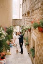 Bride and groom walk along a narrow old street decorated with blooming flowerpots Royalty Free Stock Photo