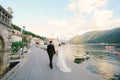 Bride and groom walk along the pier holding hands, against the backdrop of the bay, boats and ancient buildings Royalty Free Stock Photo