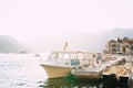 The bride and groom walk holding hands along the pier near the old town of Perast, next to them are tourist boats Royalty Free Stock Photo