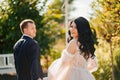 bride and groom walk holding hands through park. wedding walk. view from back