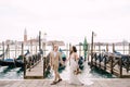 The bride and groom are walking along the gondola pier, holding hand in Venice, near Piazza San Marco, overlooking San Royalty Free Stock Photo