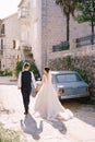 The bride and groom are walking along an old stone street, against the background of blue vintage car. Wedding couple Royalty Free Stock Photo