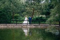 The bride and groom are walking in the green park, the man is leading his wife across the bridge, holding her by the Royalty Free Stock Photo