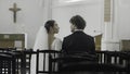 Bride and groom at the wedding ceremony in modern church. Action. Woman and man sitting together among empty seats. Royalty Free Stock Photo