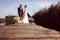 Bride and groom on wooden bridge near houses on lake