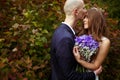 Bride hold a wedding bouqet behind her chest while groom kisses