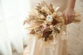 Bride holding beautiful dried flower bouquet near window at home, closeup Royalty Free Stock Photo