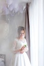 The bride holding in hand close-up the groom`s buttonhole flowers with white roses, and green and greenery. Bride`s Preparations