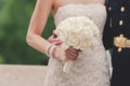 A Bride holding a ivory colored bouquet shot showing only midsection next to military jacket of husband