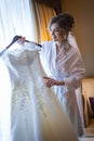 Bride holding wedding dress on a hanger near window and smiling Royalty Free Stock Photo