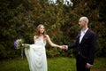 Bride holds a bouquet and a dress in one arm and groom's hand in Royalty Free Stock Photo