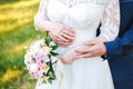 The bride holds a bouquet in her lowered hand, the groom hugs her waist from behind