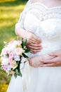 The bride holds a bouquet in her lowered hand, the groom hugs her waist from behind