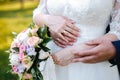 The bride holds a bouquet in her lowered hand, the groom hugs her waist from behind