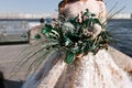 The bride is holding a bouquet of various exotic plantson a blurred background of the river and the city, selective focus