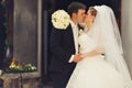 Bride holds a hand with bouquet on groom's shoulders while kissi Royalty Free Stock Photo