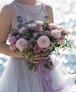 The bride holds a pink and lilac wedding bouquet in her arms against the background of the sea Royalty Free Stock Photo