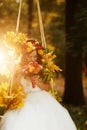 Bride holds a red wedding bouqet in her arms sitting on the swing illuminated with autumn sun