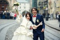 Bride holds thumbs up standing behind a groom on the city square