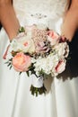 The bride holds a wedding bouquet of different flowers in her hands