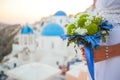 Bride holds wedding bouquet in white and green colors and blue decor against the backdrop of the sunset over Santorini, Greece Royalty Free Stock Photo