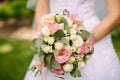 Bride holds a wedding bouquet of white and pink roses on the green background outdoors in the open air, wedding dress Royalty Free Stock Photo