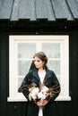 Bride in a jacket with a bouquet stands near a black wooden house. Iceland Royalty Free Stock Photo