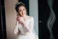 The bride in a lacy white dress and veil is going to the ceremony. Portrait of a girl putting on earrings and smiling. Royalty Free Stock Photo