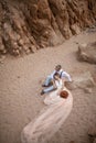 Bride in long dress and groom sit and hold hands in canyon on sand. Top view. Royalty Free Stock Photo