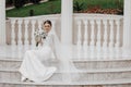 The bride in a long dress sits near white Roman-style columns.