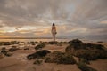 Bride in a long white wedding dress stands on the on Bali ocean beach at sunset