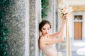 Bride lowered her eyes, leaning against a pillar with raised hands with a bouquet of flowers. Lake Como