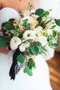 Bride in a luxurious wedding dress holding a wedding bouquet decorated with a black ribbon made of roses