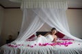 Bride is lying on a white bed in rose petals in the hotel