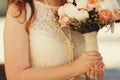 Bride in pearls holds a wedding bouquet decotated with lace