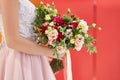 Bride in a pink dress is standing with a beautiful bouquet of carnations and roses on a red background Royalty Free Stock Photo